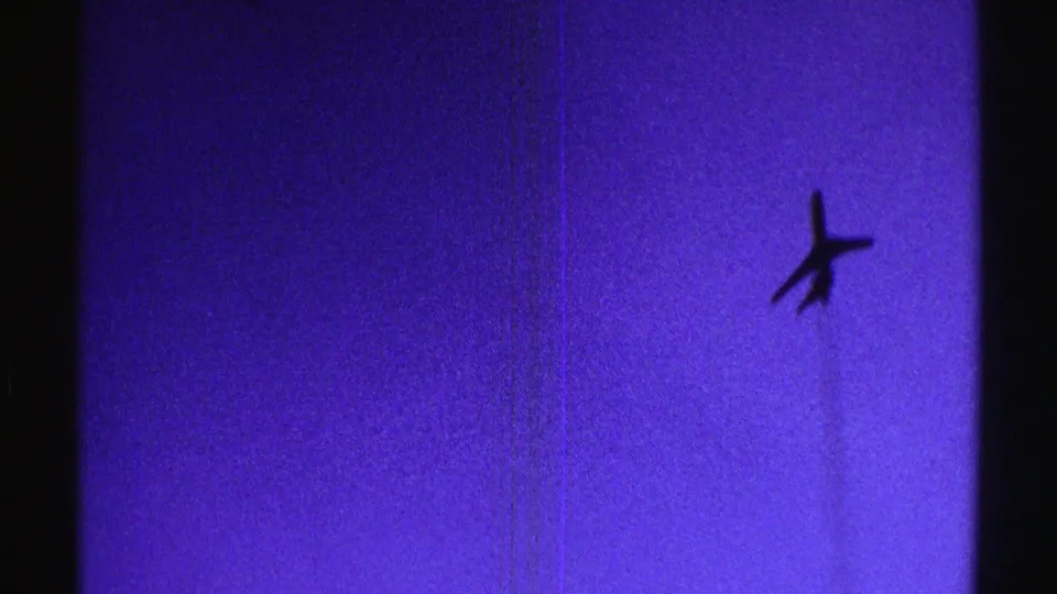 1969 Nebraska 8mm frame showing an airplane silhouette overhead against a saturated blue-violet sky.