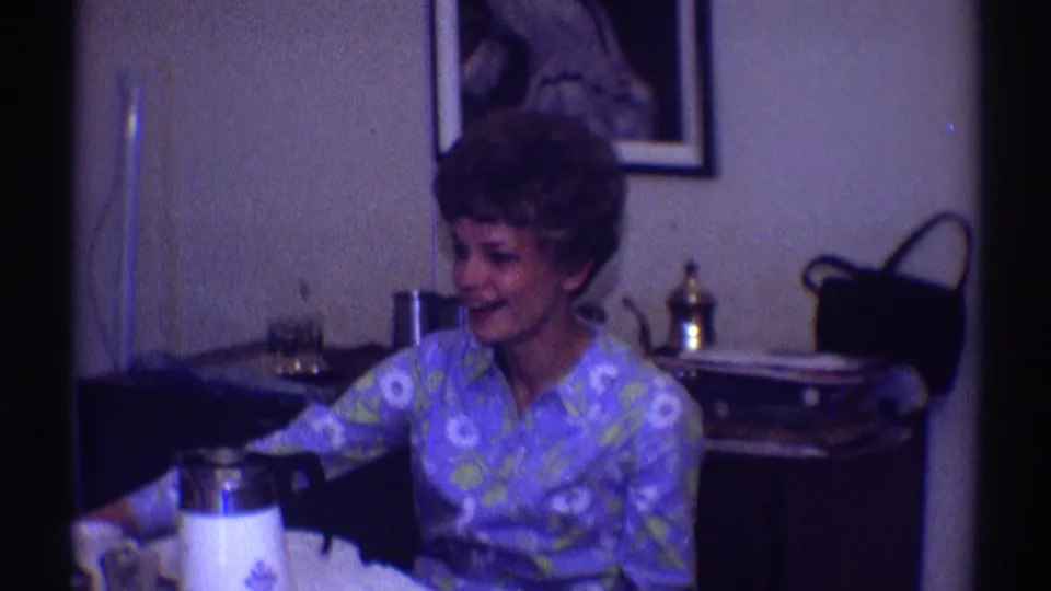 The woman sits at the table in the Clarendon Hills interior, smiling beside a white thermos, framed wall art, furniture, and small objects.