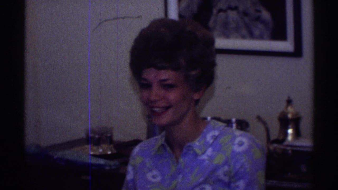 1969 Clarendon Hills home-movie frame showing two adult women seated in a dim domestic interior with framed art and a lamp behind them.