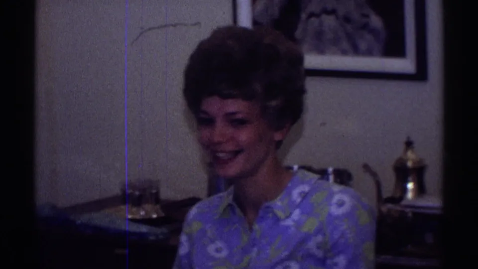 1969 Clarendon Hills home-movie frame showing two adult women seated in a dim domestic interior with framed art and a lamp behind them.