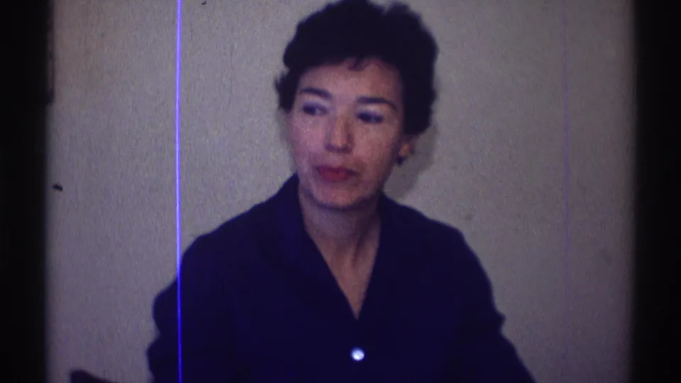 The seated woman in a dark collared top looks off camera inside the Clarendon Hills home interior, with visible 8mm grain and blue line artifact.