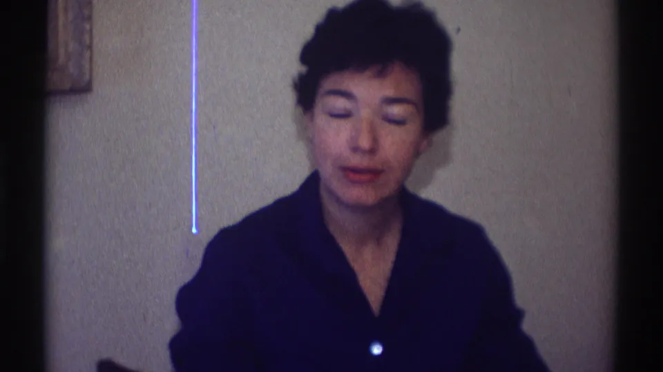 Adult woman seated in a dark collared top lowers her eyes in a quiet 1969 Clarendon Hills home-movie frame.