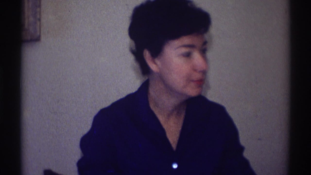 In Clarendon Hills, Illinois, 1969, a woman in a dark blue collared shirt sits indoors beside a plain wall and looks off-camera.