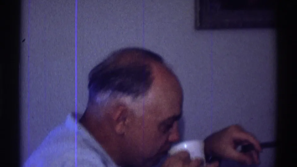 A profile view shows the seated man leaning down with a small cup and cigarette in a dim blue-toned private room.