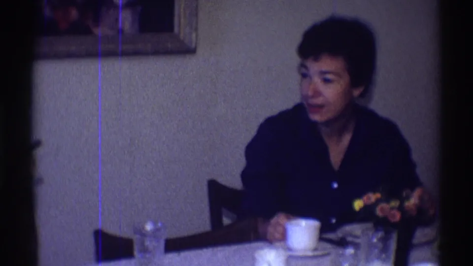 A woman sits at a table in a Clarendon Hills interior, with coffee cup, glassware, flowers, and framed wall pictures visible.