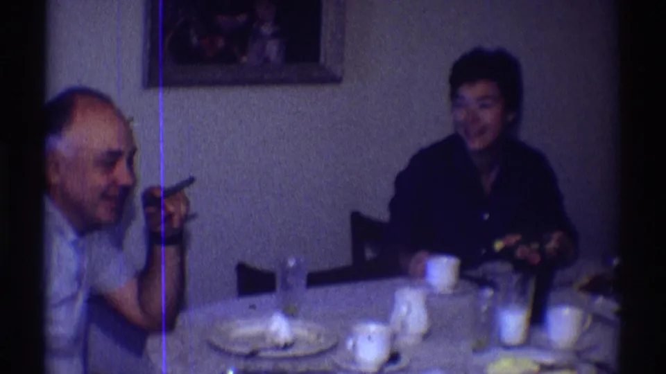 A man with a cigar and a woman sit at a Clarendon Hills dining table with cups, plates, glasses, and framed wall art behind them.