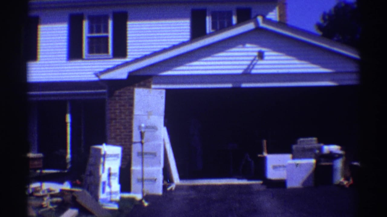 White two-story suburban house with boxes and household items outside the garage.