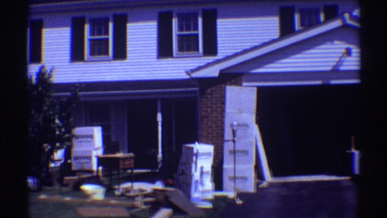 Front of a suburban house with stacked boxes, furniture, and an open garage area.