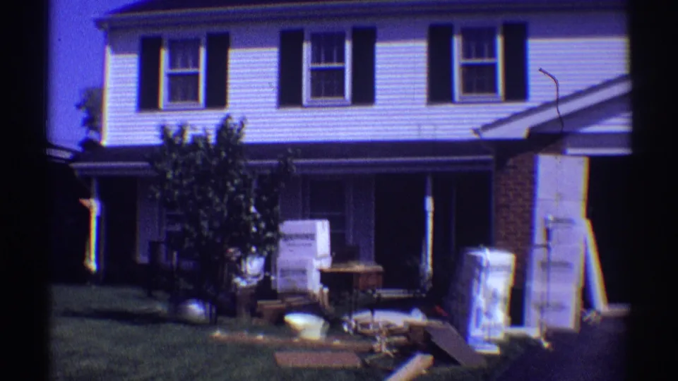 Clarendon Hills home-movie frame of a two-story house with household goods, boxes, and furniture spread across the front yard and driveway.