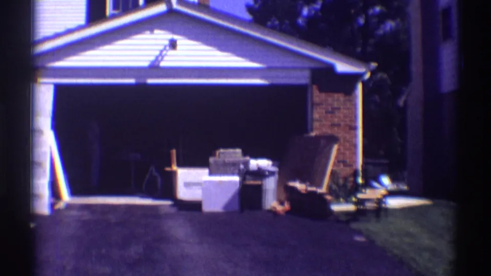 1969 Clarendon Hills frame of a white house garage with household items staged outside on the driveway and lawn during a move.
