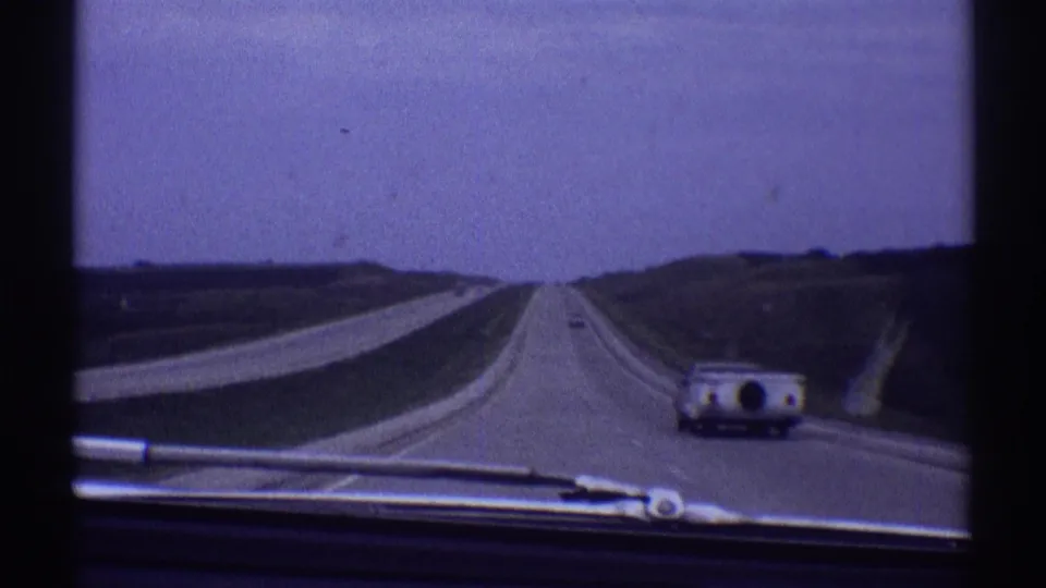1969 home-movie view from inside a car on a straight highway near Clarendon Hills, Illinois, with a camper-towing vehicle ahead.