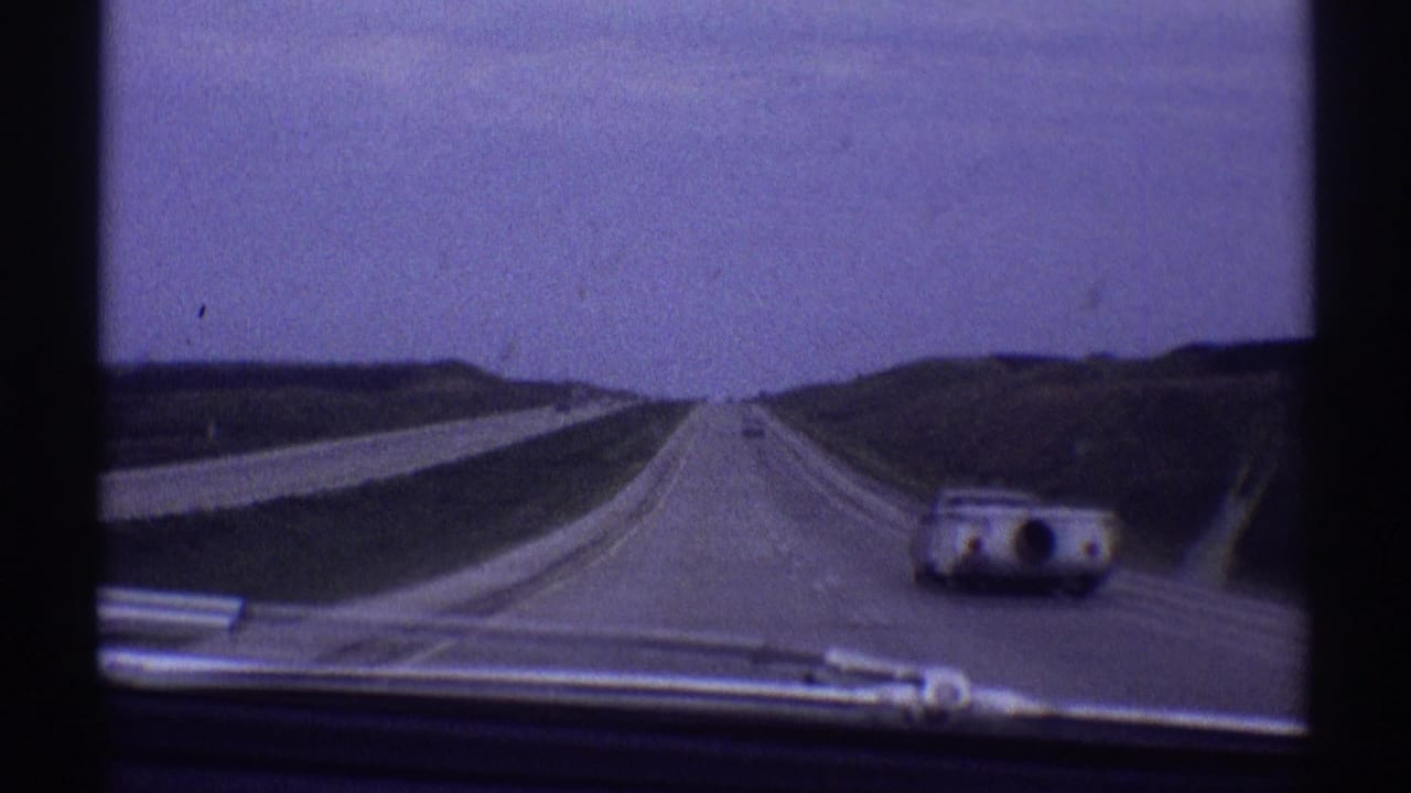 Vehicle-mounted 8mm view of a 1969 highway scene, with a rounded camper trailer car visible to the right and open road ahead.