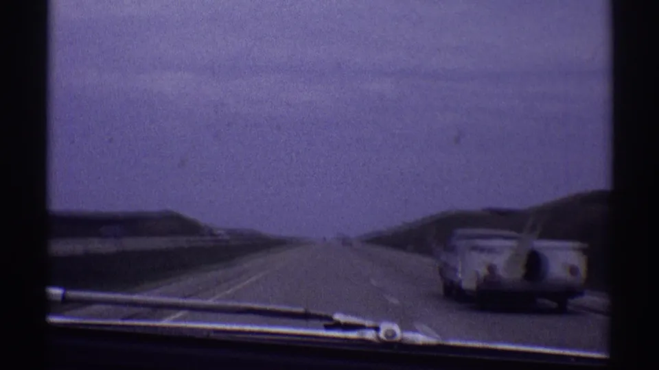 1969 8mm windshield view in Clarendon Hills, Illinois, showing a grey car towing a white trailer on a multi-lane highway.