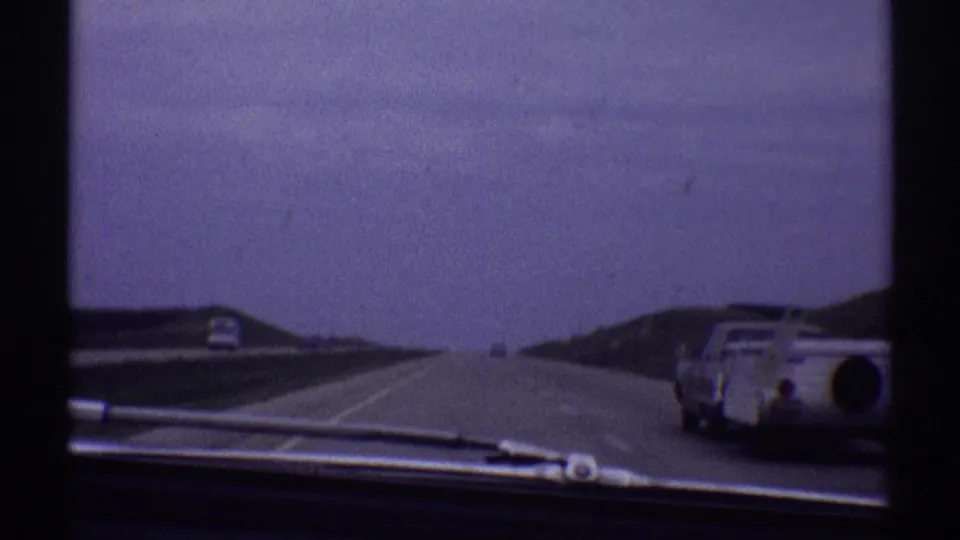 Windshield-shot 1969 road footage with the trailer-towing car moving toward the right side of the frame.