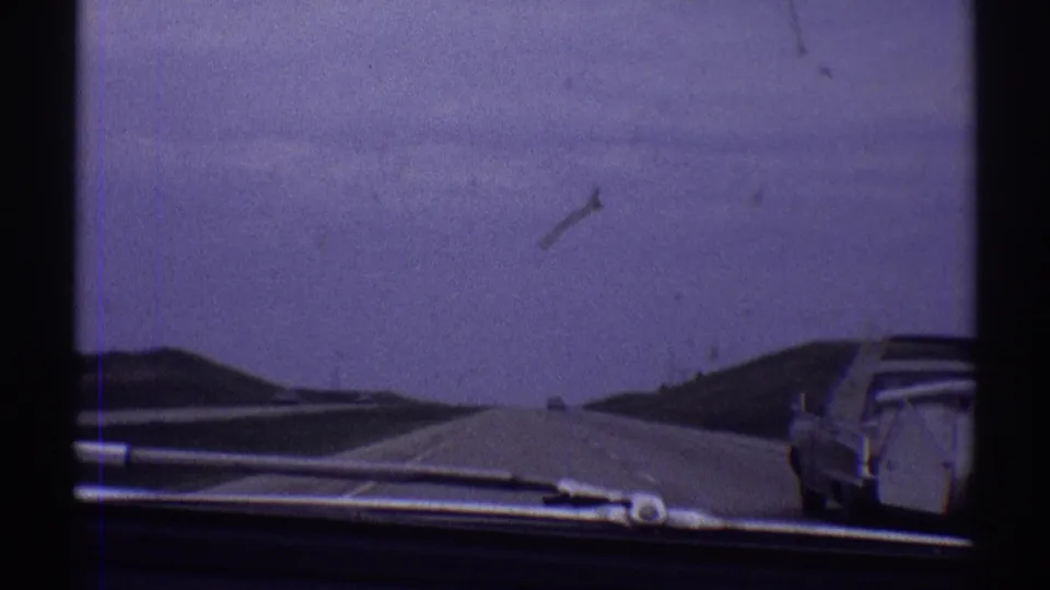 Late-1960s 8mm highway shot looking forward as the car towing a trailer exits the right side of frame.