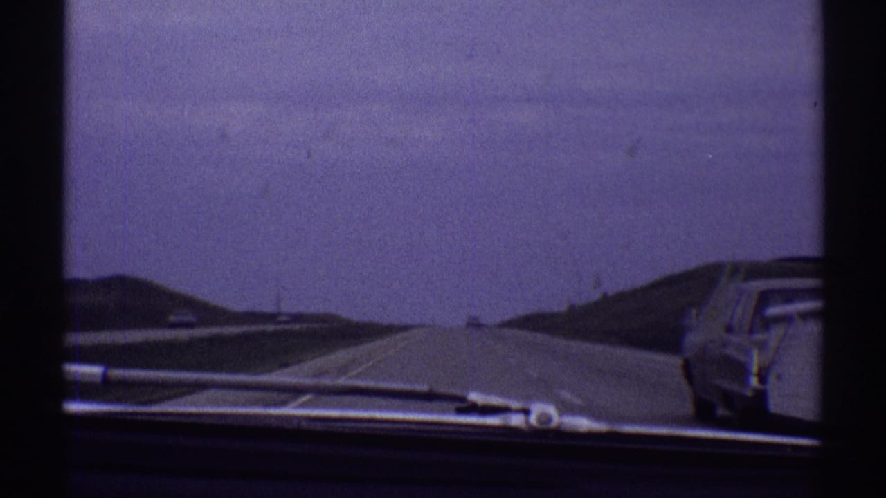 Open highway seen through a car windshield with a sedan near the roadside.