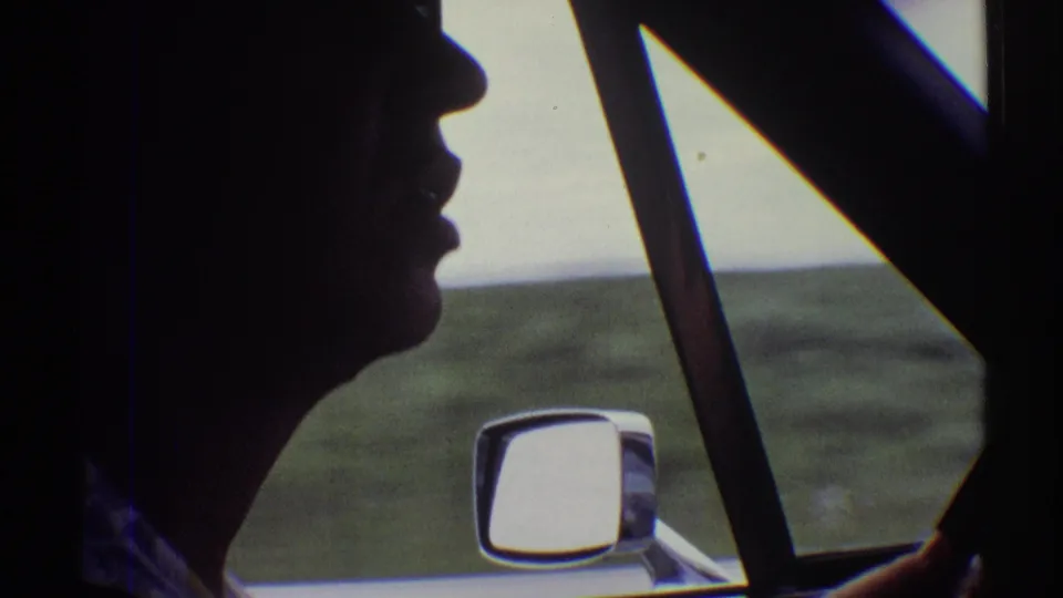1969 Clarendon Hills home-movie frame showing a driver in dark profile beside a car window, side mirror, and open landscape.