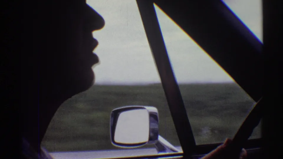 1969 Illinois car-interior view with the driver's profile in silhouette, a hand near the wheel, and fields passing outside.