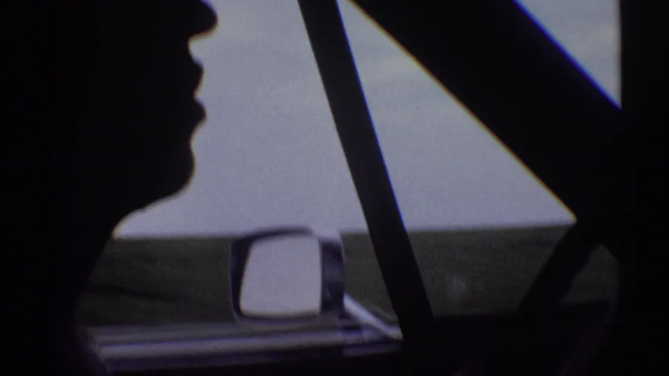 Close 1969 home-movie view of a driver in silhouette, framed by the car window and side mirror against a bright exterior.