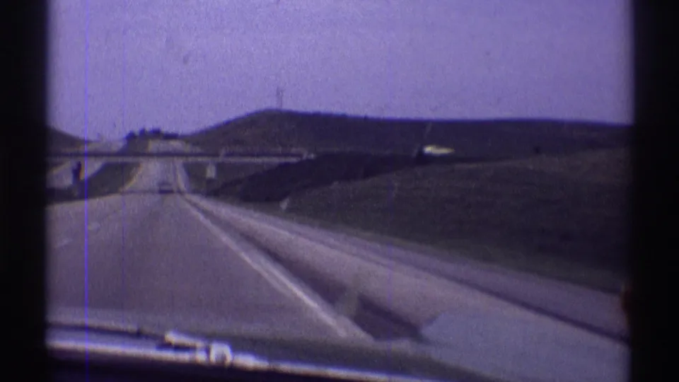 Forward-facing 1969 home-movie view along an open Illinois highway toward an overpass, with lanes, grassy embankments, and pale sky visible.