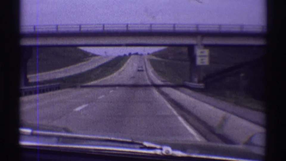 1969 8mm windshield view from a car on a highway near Clarendon Hills, Illinois, approaching and passing under a concrete overpass.
