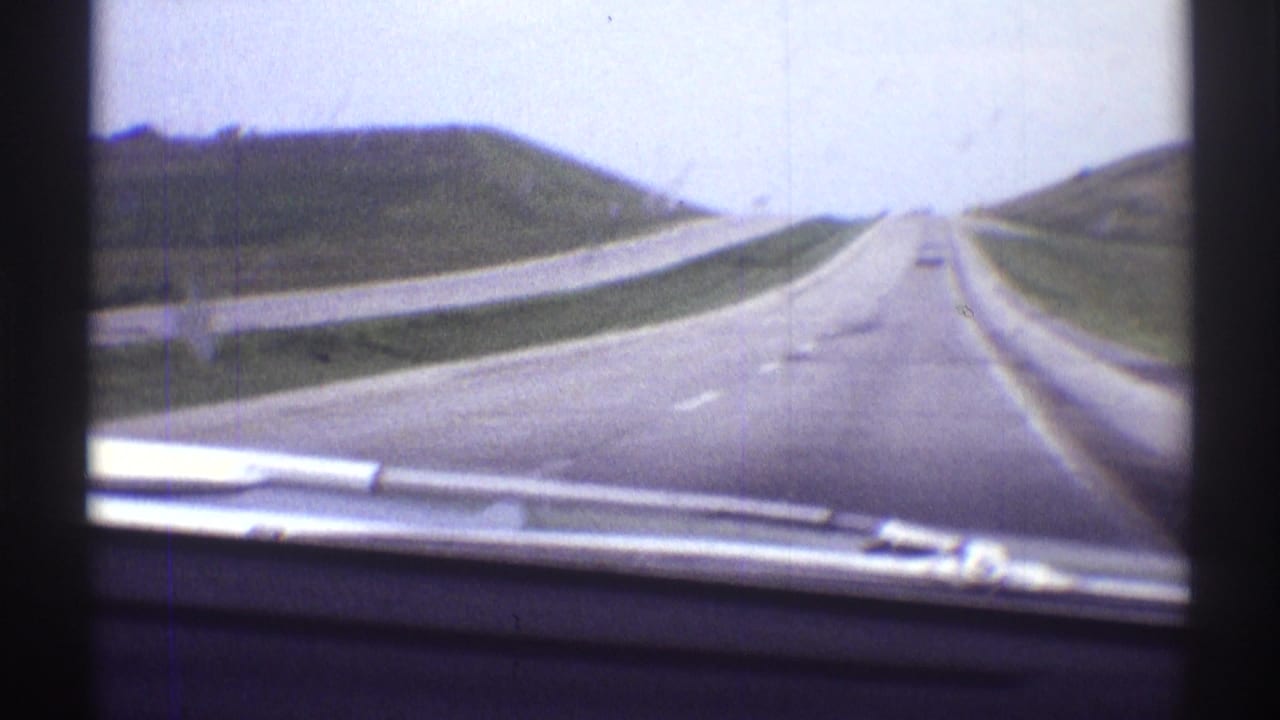 Open highway seen through a car windshield with grassy slopes on both sides.