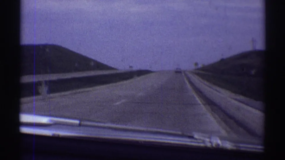Late-1960s 8mm windshield view on a highway near Clarendon Hills, Illinois, showing sparse traffic and grassy roadside banks.