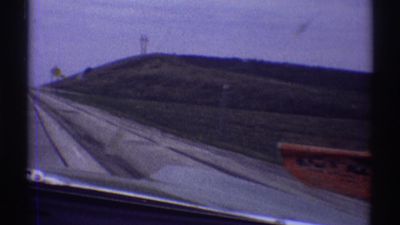 1969 Illinois driving footage shows the road edge, car hood, rural slope, utility poles, and a partially blurred red sign outside the window.