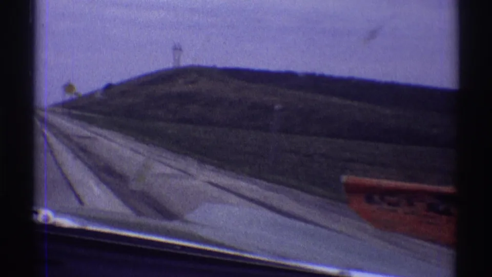 1969 Illinois driving footage shows the road edge, car hood, rural slope, utility poles, and a partially blurred red sign outside the window.