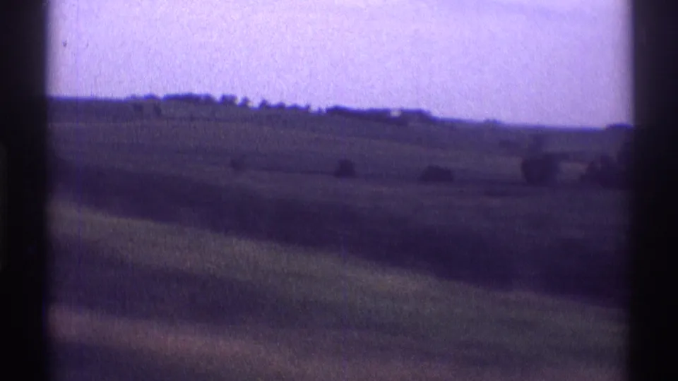 Passing 1969 home-movie frame of sloped farmland near Clarendon Hills with a distant tree line and visible 8mm frame edges.