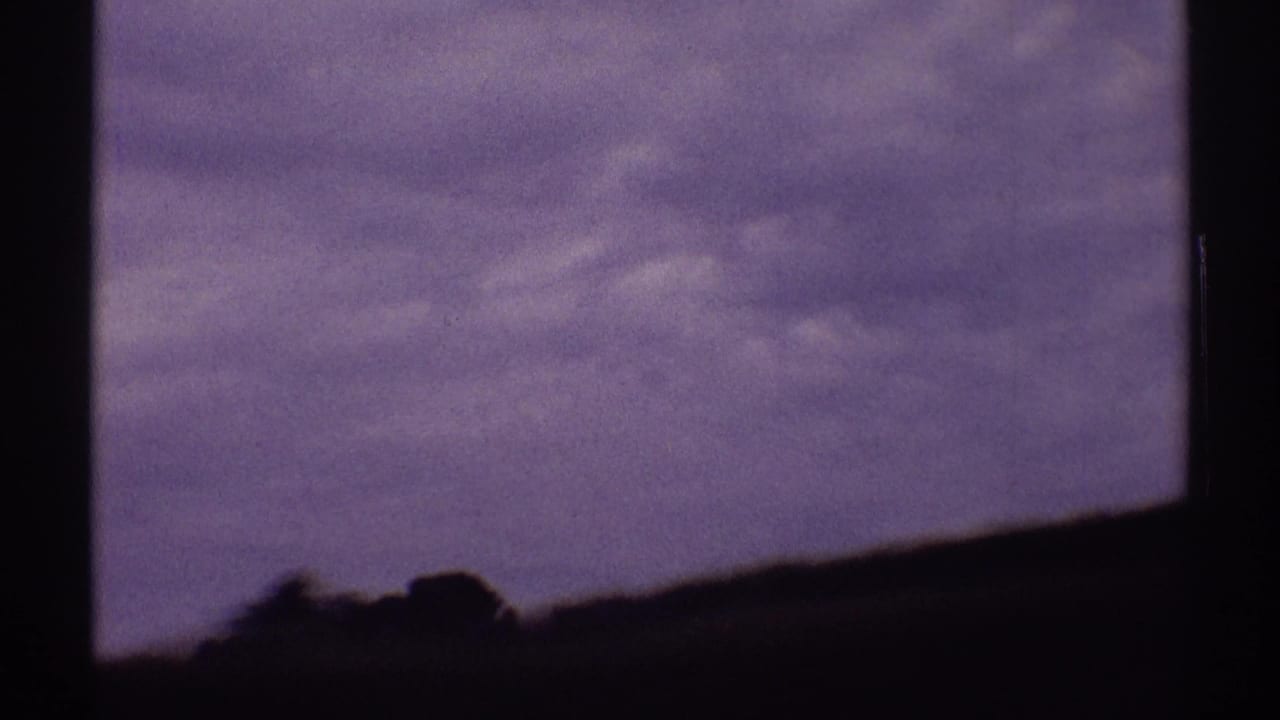 1969 8mm home-movie frame from Illinois showing a dark windshield view toward a low rural horizon under a muted sky.