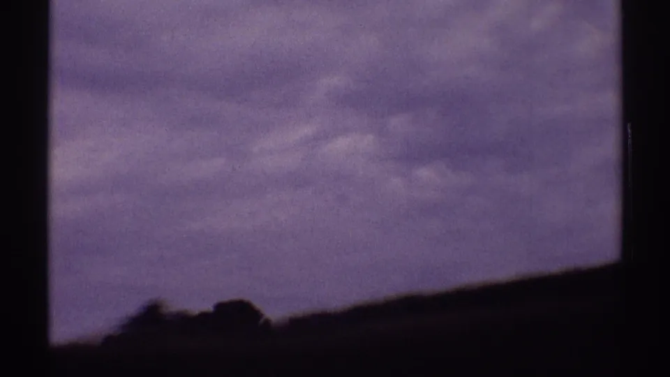 1969 8mm home-movie frame from Illinois showing a dark windshield view toward a low rural horizon under a muted sky.