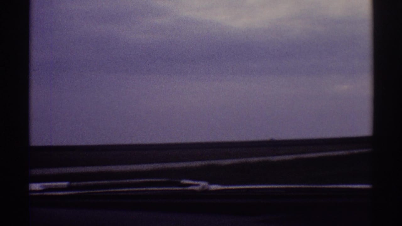 1969 Clarendon Hills home-movie frame showing purple-gray clouds through a moving car window, bordered by dark interior trim.