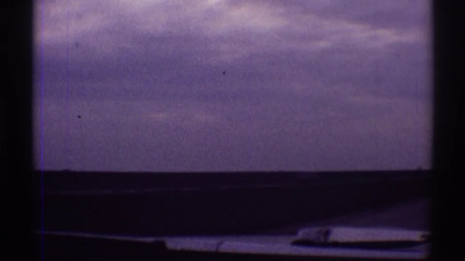 Passenger-view 8mm frame from 1969 Clarendon Hills showing muted clouds beyond a car window and dark windshield trim.
