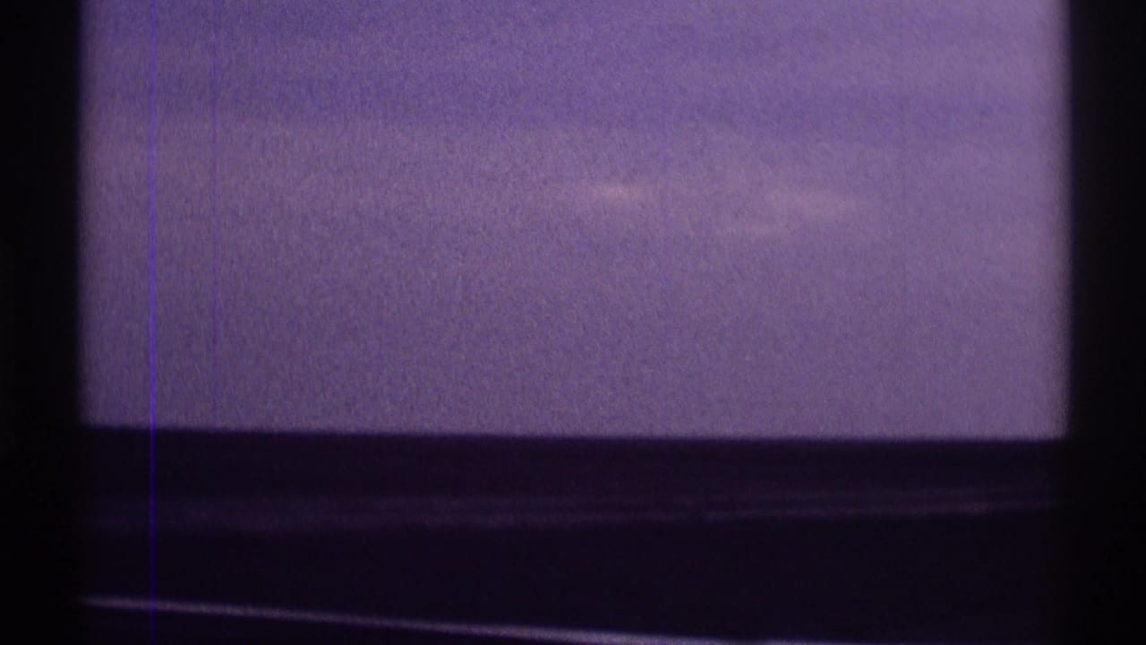 Purple-blue sky seen through dark window-like framing with film grain and scratches.