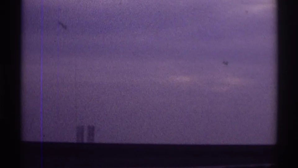 Final 1969 Clarendon Hills frame with purple-tinted sky, dark window-like borders, and faint distant shapes near the horizon.