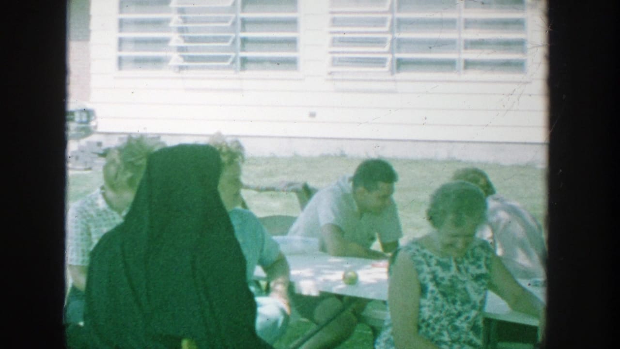 Group seated outdoors near a table, including a figure in a dark religious habit.