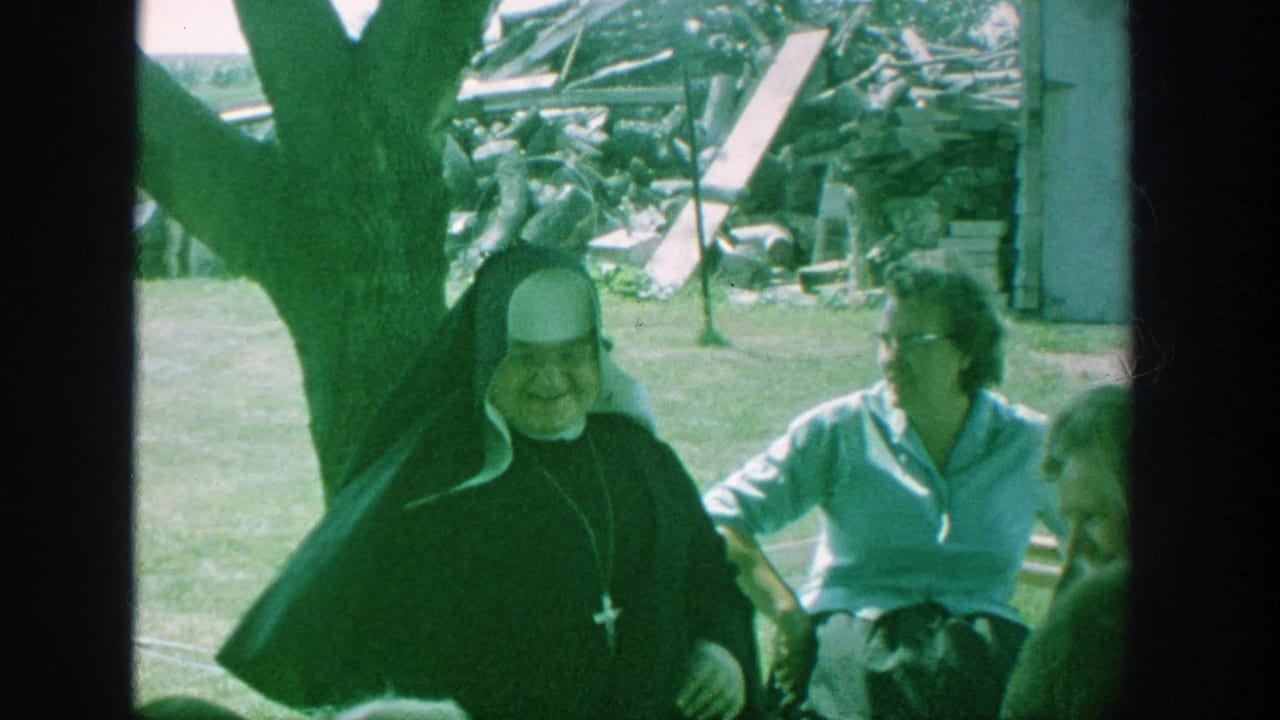 Nun in a black habit sits outdoors with elderly women on lawn chairs.