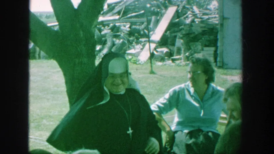 In Michigan 1964 home-movie footage, a nun in a black habit sits smiling with elderly women gathered in a grassy yard.