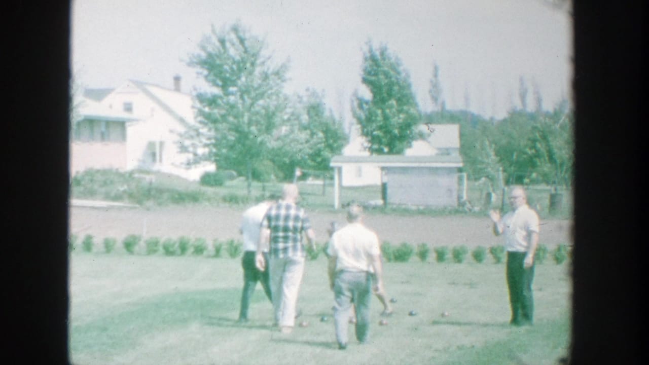 Five men stand on a grassy backyard lawn near scattered bocce balls.