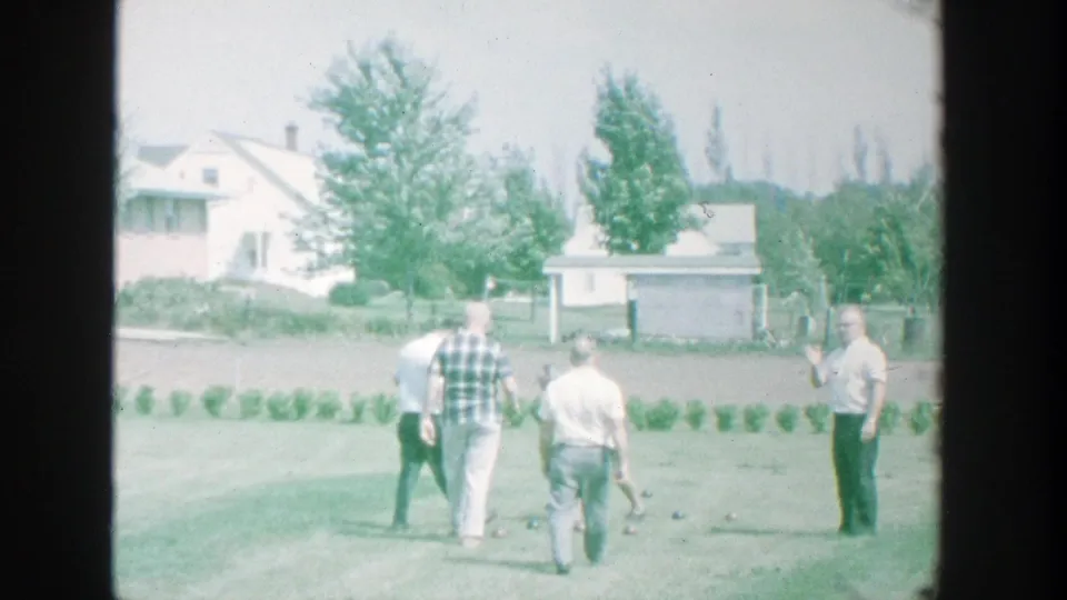 1964 Michigan home-movie frame of five men in casual clothes playing bocce on a sunny suburban lawn.