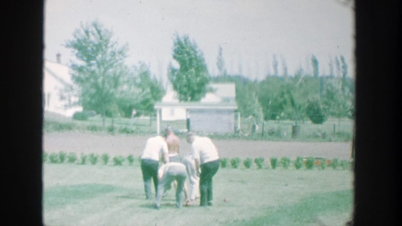 1964 Michigan home-movie still of men checking bocce balls on a suburban backyard lawn.