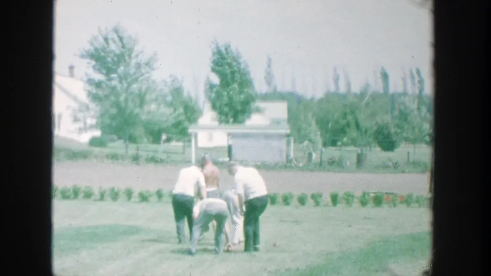 1964 Michigan home-movie still of men checking bocce balls on a suburban backyard lawn.