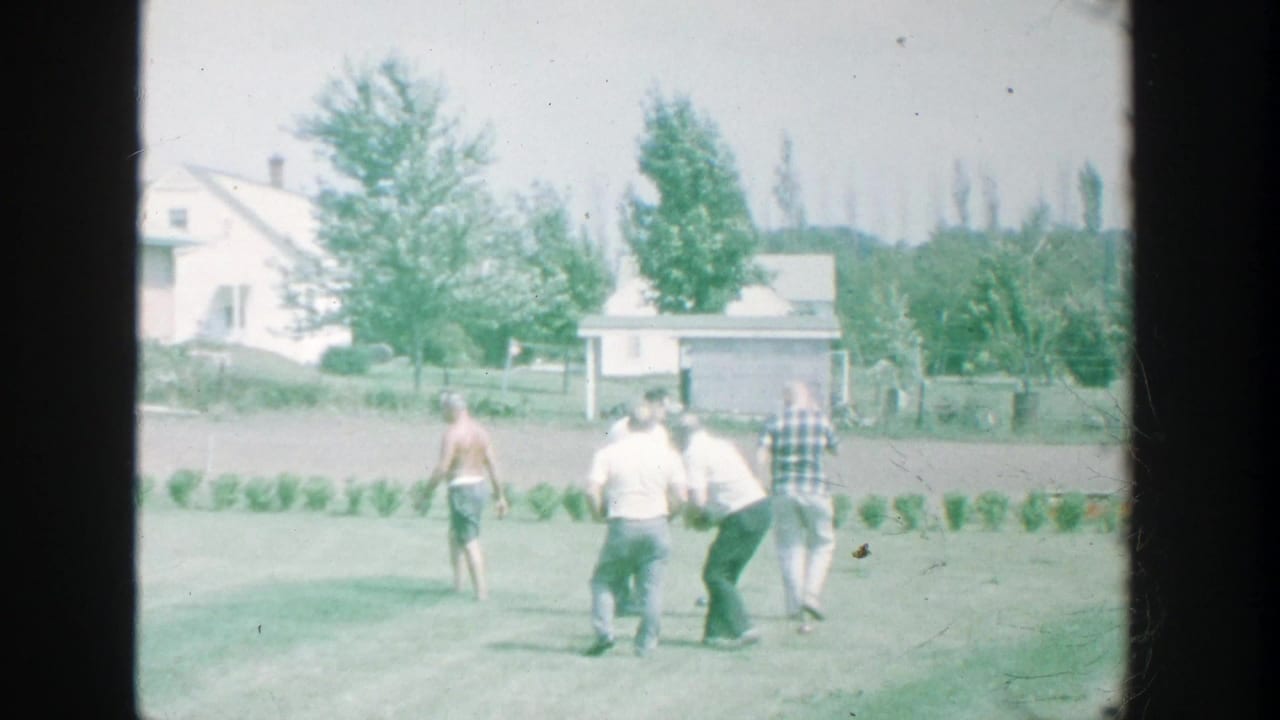 1964 Michigan backyard frame showing men moving around the lawn during a casual bocce game.