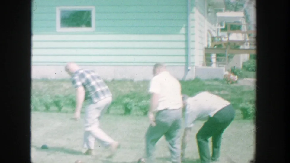 Men in casual clothing move across a Michigan backyard beside a light blue house, with small objects visible on the grass.