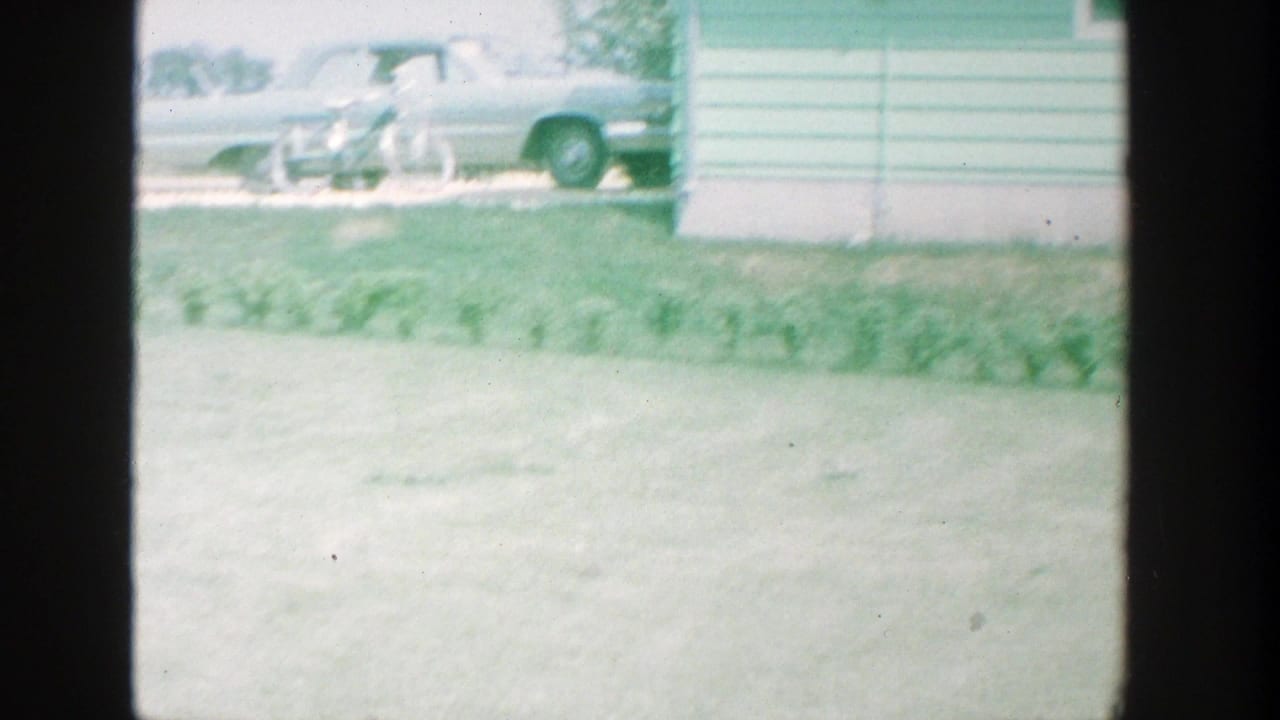 A classic sedan is parked near a house beyond a wide grassy yard.