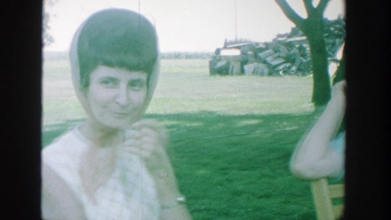 Woman in a white dress smiles near another person raising an arm by a tree.