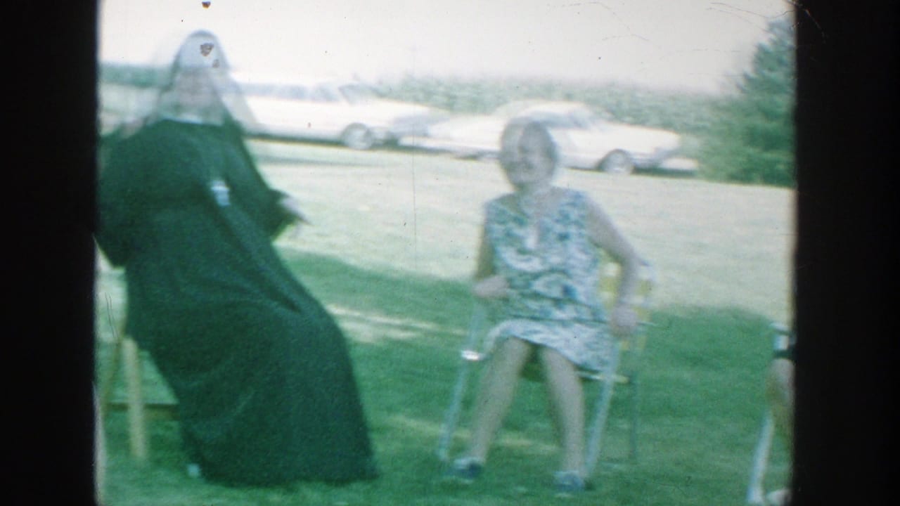 A nun and a woman in a floral dress sit on lawn chairs in a grassy park.