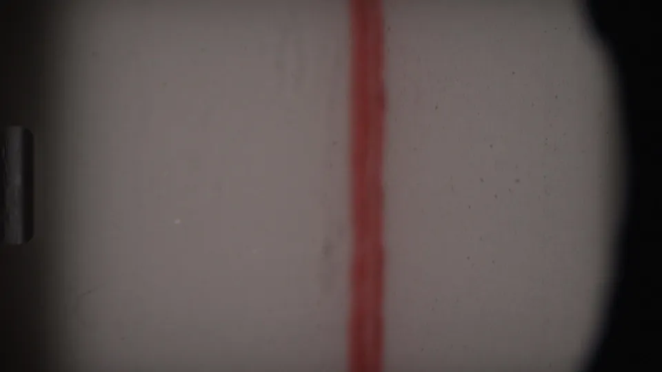 Final 1969 Angola 8mm frame is largely abstract, showing pale film surface, a red vertical line, dust, and dark rounded edge.