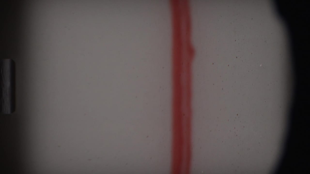 1969 Angola-attributed 8mm frame showing a pale surface crossed by a red vertical mark, with dark frame edges, grain, and dust.